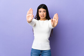 Young brunette woman over isolated purple background making stop gesture and disappointed