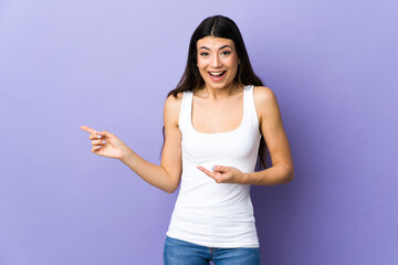 Young brunette woman over isolated purple background surprised and pointing side