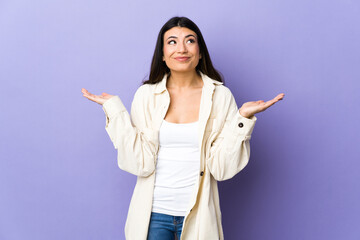 Young brunette woman over isolated purple background having doubts while raising hands