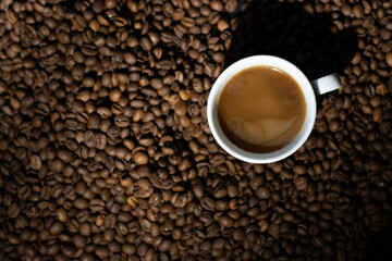 A cup of black coffee with milk is on top of roasted coffee beans.