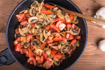Cooking mushroom ragout - sliced champignons, tomatoes and onions are fried in a pan, top view. Healthy vegetarian cuisine