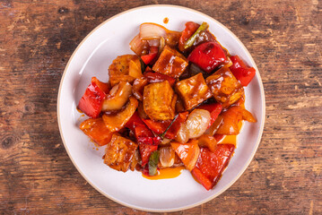 Tofu with peppers and onions in a spicy sauce, portion in a plate, top view. Stir-fry dish