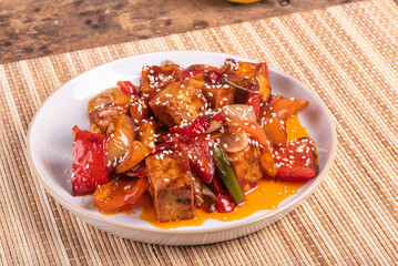 Tofu with peppers and onions in a spicy sauce with sesame seeds, portion in a plate, close-up. Stir-fry dish