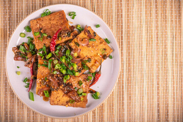 Fried tofu with onions in a hot sauce with sesame seeds in a plate, top view, copy space. Korean and Chinese vegetarian food.