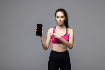 Portrait of a smiling fitness woman pointing finger at blank screen mobile phone isolated over white background