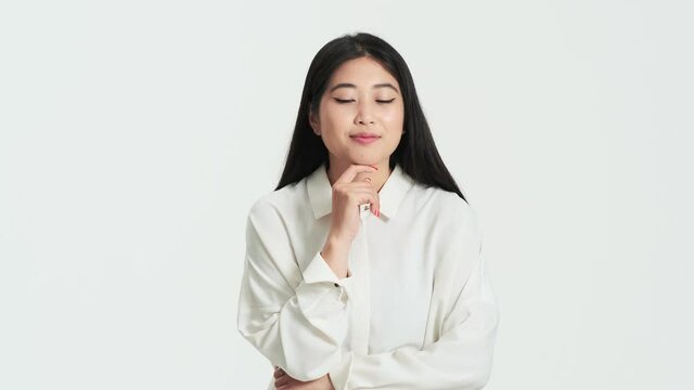 Pleased asian korean woman pondering while coming up with an idea standing isolated over white background in the studio