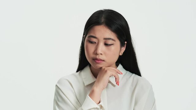 Close-up view of a serious asian korean woman thinking about something standing isolated over white background in the studio