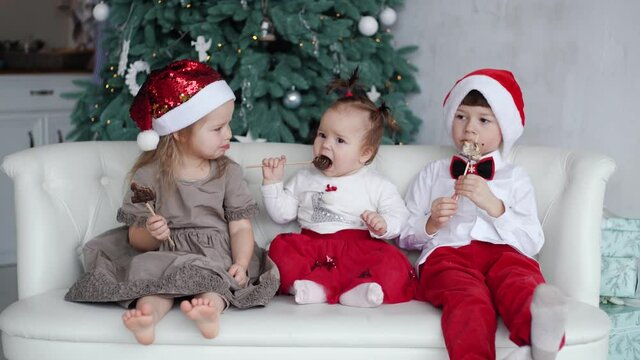 4k video portrait of real family in sweet holiday Christmas interior. Kids eating chocolate sweets happily sitting on white couch