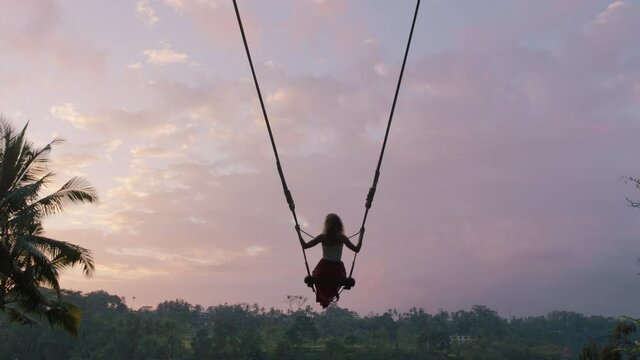 tourist woman swinging over tropical jungle at sunrise travel girl enjoying exotic vacation sitting on swing in having fun holiday lifestyle freedom 4k