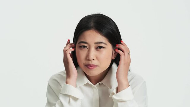 Close-up view of a beautiful asian korean woman looking to the camera as to the mirror standing isolated over white background in the studio