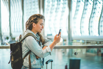 A beautiful caucasian young woman using mobile phone at airport to buy tickets online, book hotel,...