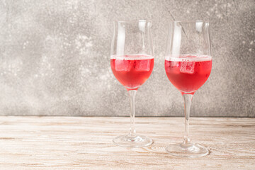 Two glasses of rose cocktails. Sparkling red cocktail with ice on wooden table made at home. Homemade red cocktails