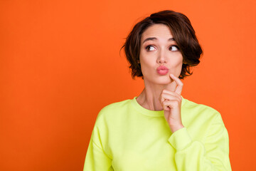 Photo of cheerful young happy woman look empty space minded lips pouted isolated on orange color background