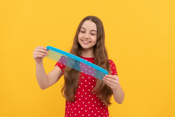 happy kid brushing long hair with comb on yellow background, haircare