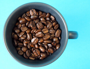 close by, a dark gray mug filled with roasted whole coffee beans stands on a blue background. top view