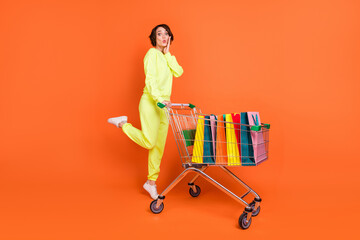 Full length body size view of nice amazed funny girl carrying cart bags clothes things pout lips isolated over bright orange color background