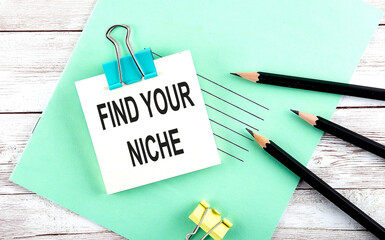 Text FIND YOUR NICHE on the short note with pencils on the wooden background