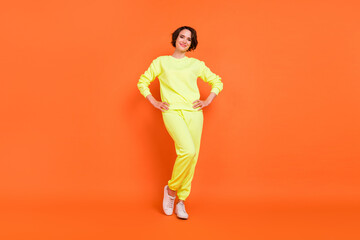 Fototapeta na wymiar Full length body size view of attractive cheerful content girl posing hands on hips isolated over bright orange color background