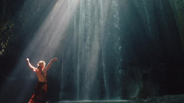 dancing woman in waterfall cave splashing water wearing beautiful dress enjoying nature dance feeling spiritual freedom 4k