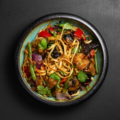 Udon stir-fry noodles bowl and vegetables on black stone background. Asian cuisine. Top view. Copy space.