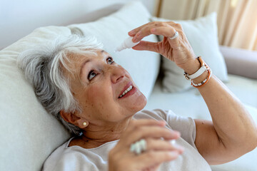 A sick old woman suffering from irritated eye, optical symptoms. A senior woman applying eye drop...