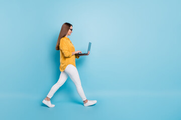 Full length profile side photo of attractive woman hold laptop walk empty space isolated on blue color background