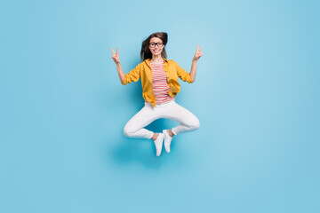 Full body photo of young woman happy positive smile show peace cool v-sign jump up isolated over blue color background