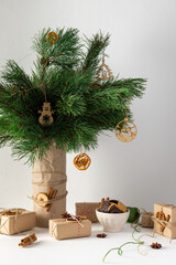 Festive christmas table, vase with pine branches and toys, gift boxes and a plate of chocolate cookies, dried citrus fruits, cinnamon with star anise
