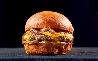Juicy burger with beef, cheese, caramelized onions and tomato, sauce on a dark background.