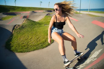 Poster Attractive young woman riding longboard. Pretty sporty girl in sunglasses with skateboard on special riding area, doing trick. Sport, hobby, active lifestyle concept © KAMPUS
