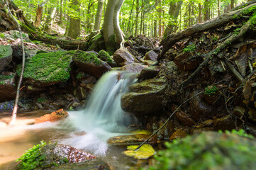 Naklejka na ściany i meble Small forest waterfall with blurred water