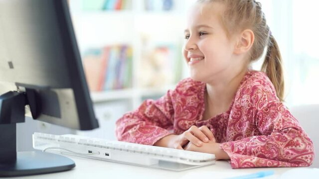 Happy school girl sitting in front of computer during distant lesson