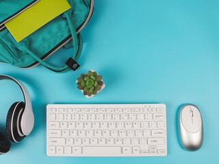 Obraz na płótnie Canvas flat lay of computer keyboard, headphones, mouse, school backpack and cactus on blue background with copy space. Online learning concept.