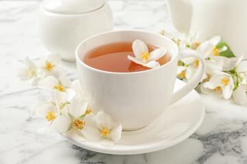 Cup of aromatic jasmine tea and fresh flowers on white marble table