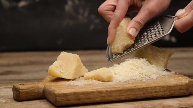 Woman using grater on parmesan cheese piece on dark background