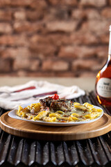 fettucine with white sauce, beef, beef medallion, mozzarella cheese and fresh basil on a white plate, red wine, black grill and rustic wall