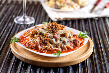 Spaghetti pasta with tomato sauce, meat, mozzarella cheese and fresh basil in deep white dish, red wine, on a black grill.