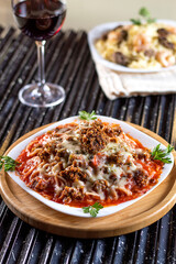 Spaghetti pasta with tomato sauce, meat, mozzarella cheese and fresh basil in deep white dish, red wine, on a black grill.