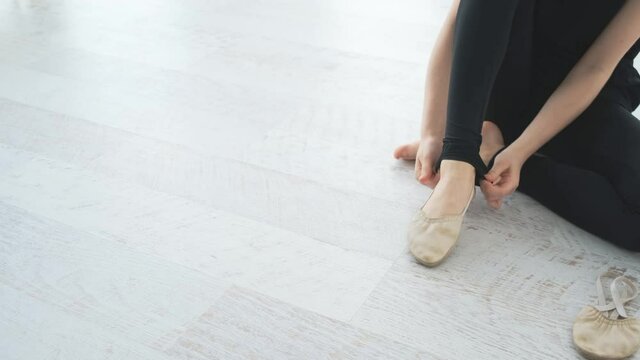 Girl wears ballet shoes in white room. Ballerina in black outfit and beige pointe