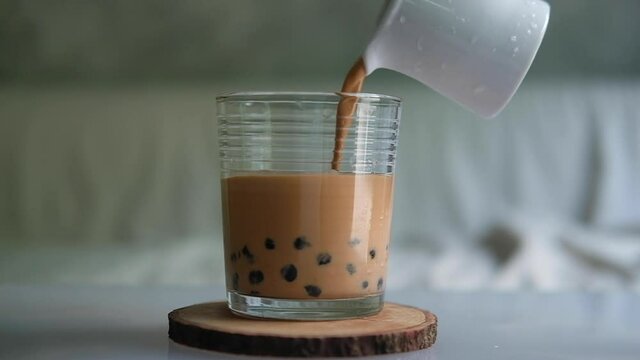 Pouring Thai milk tea with tapioca pearl bubble in glass cup. Slow motion