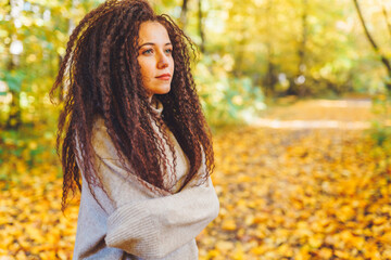 Beautiful afro-haired woman wearing warm sweater walk in autumn park at sunny warm day. Portrait of woman outdoor. Copyspace