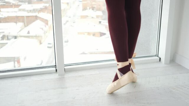 Ballerina legs in beige pointe shoes during dance practice. Girl dancing near the window