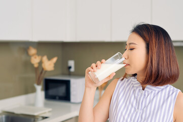 Portrait of young Asian woman drinking milk while standing in the kitchen.