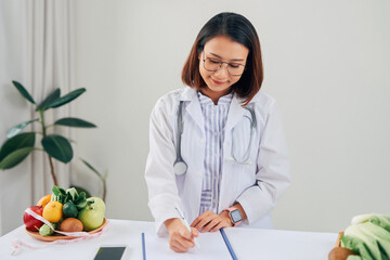Portrait of young smiling female nutritionist in the consultation room. Dietitian working on diet plan.