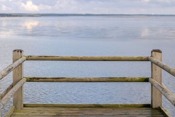 Fototapeta premium A wooden pier by a river, pond, lake with blue shiny water. Location for walks of city dwellers, relaxation outdoors. Rope fence near the lake
