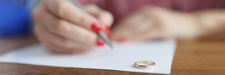 Woman hand writing declaration of divorce on background of wedding rings closeup