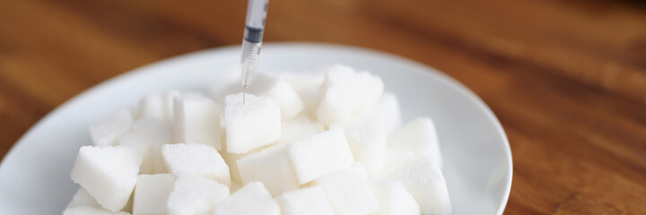 Insulin syringe inserting into lump of sugar on plate closeup
