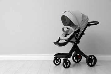 Baby carriage. Modern pram near light grey wall, space for text - Powered by Adobe