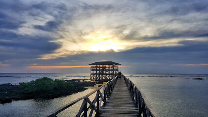 Long wooden pier with an alcove under a cloudy dark sunset sky