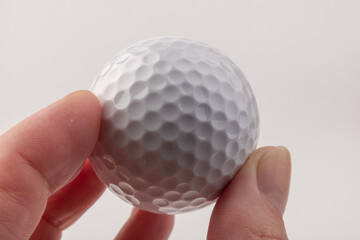 female hand holding golf ball on light background. The white color of plastic ball is popular in the game